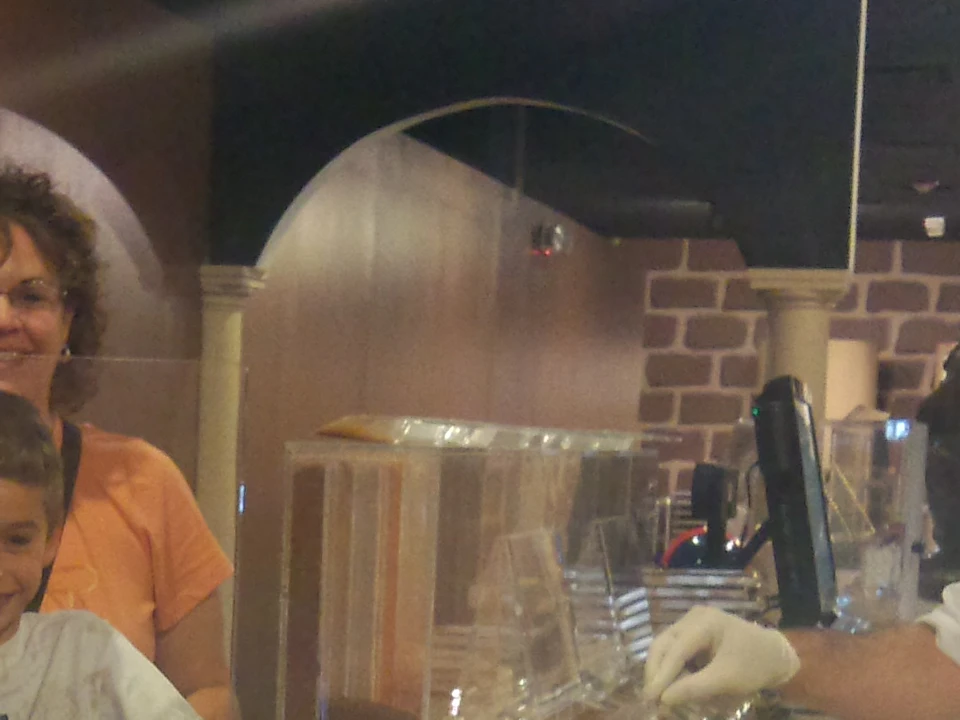 Three smiling children and an adult standing behind a counter with ice cream machines and a gloved server in the background.