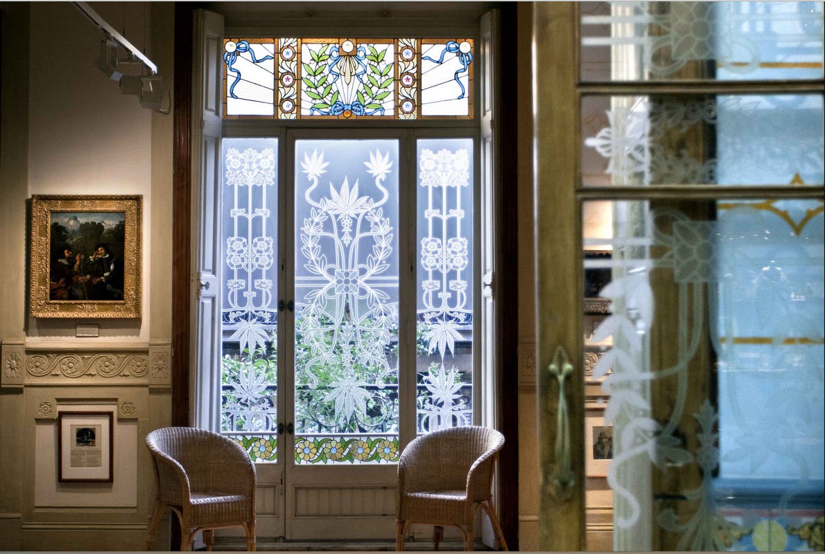 Wood-framed glass doors with intricate floral designs, stained glass at the top, and two wicker chairs in a charming room setting.