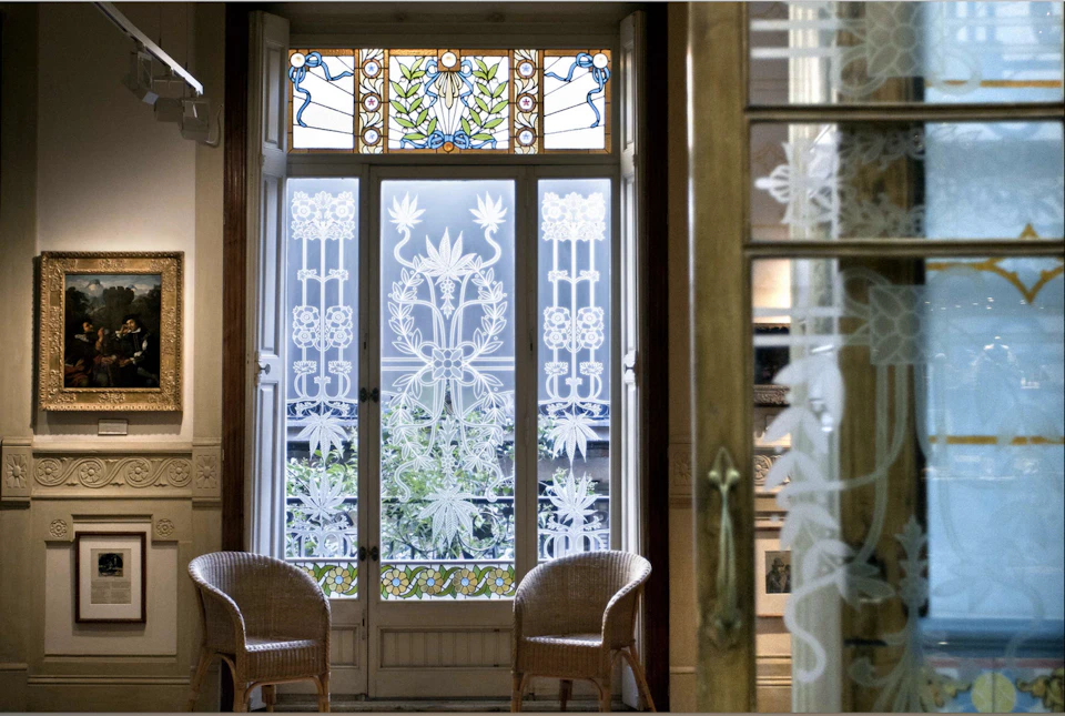 Wood-framed glass doors with intricate floral designs, stained glass at the top, and two wicker chairs in a charming room setting.