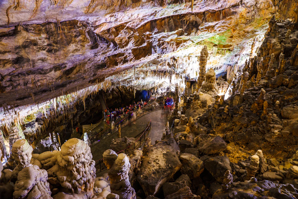 A group of people touring an illuminated cave with stalactites and stalagmites, walking along a designated path.