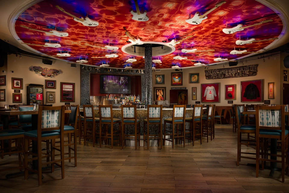 A bar with a circular counter, numerous stools, a colorful guitar-themed ceiling, and rock memorabilia on the walls.