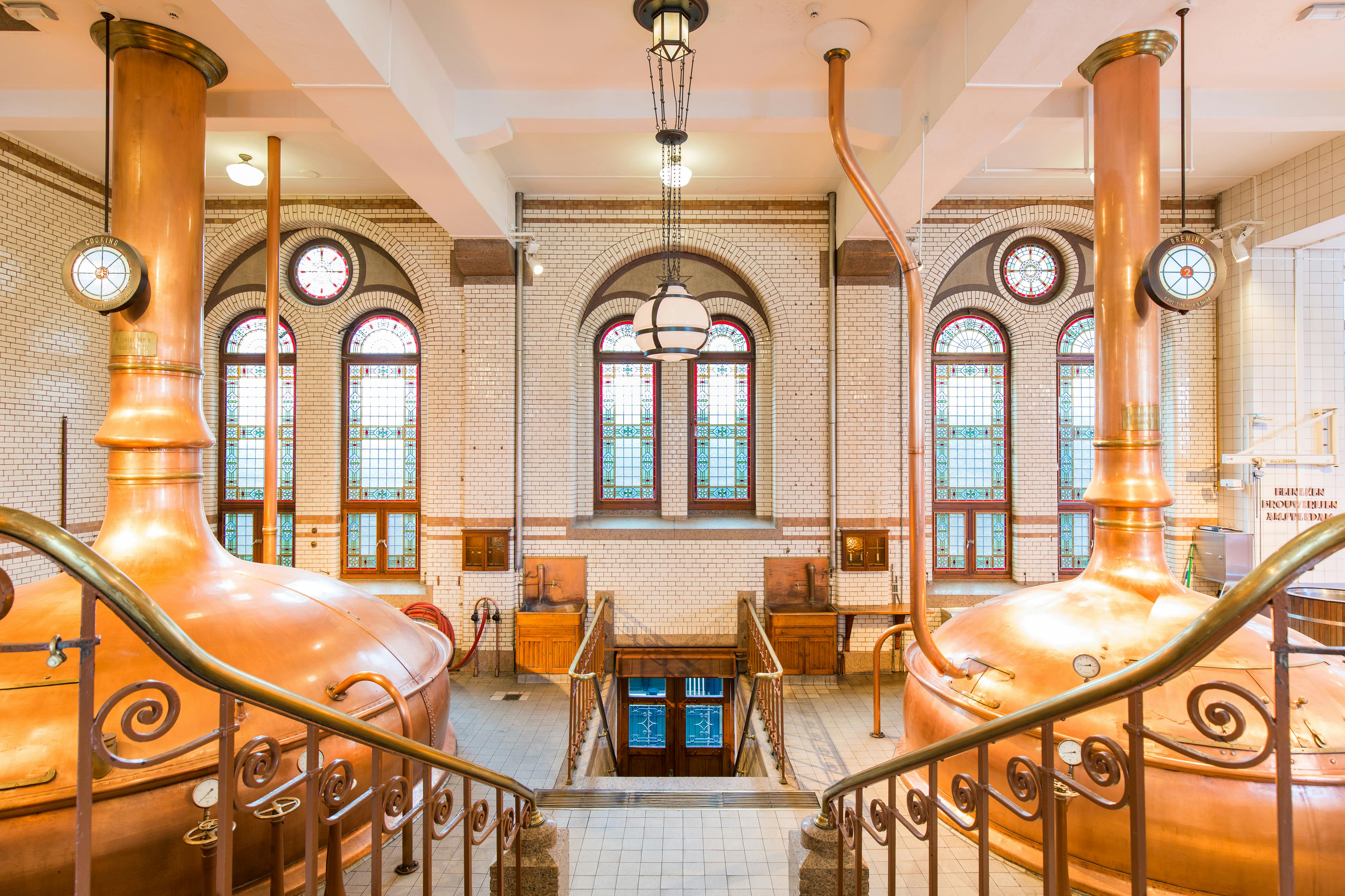 明亮的啤酒厂内部，配有大型铜制水壶、华丽的窗户和通往下面一扇门的楼梯。