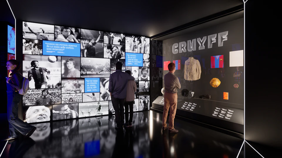 Three people in a museum exhibit, looking at a display dedicated to "Cruyff," featuring memorabilia, trophies, and photographs.