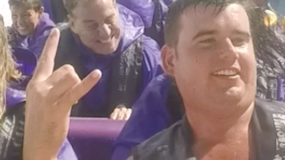 People on a boat ride wearing life jackets, with water splashing around them, some raising their hands and making gestures.
