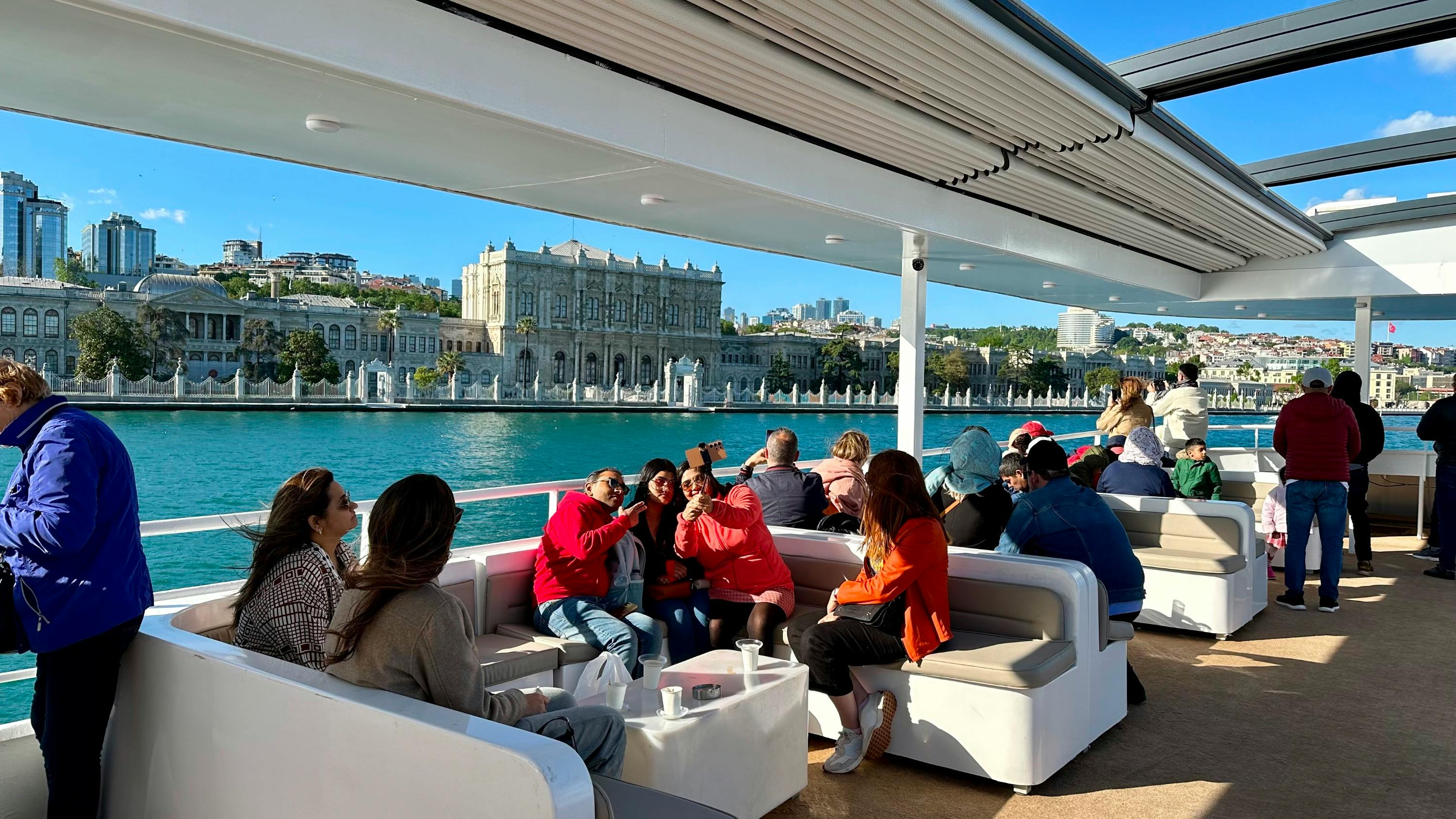 People enjoying a boat ride with a grand historical building visible across the water under a clear blue sky.