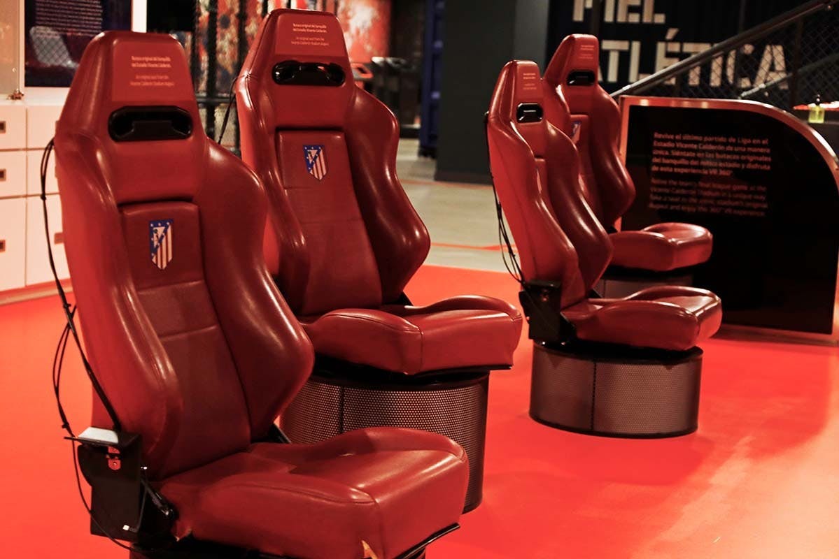 Vier rode, beklede stoelen op een rij, elk met een logo en geplaatst op een rode vloer.