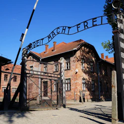 Brick buildings behind a black metal gate with the sign "Arbeit Macht Frei" under a clear blue sky.