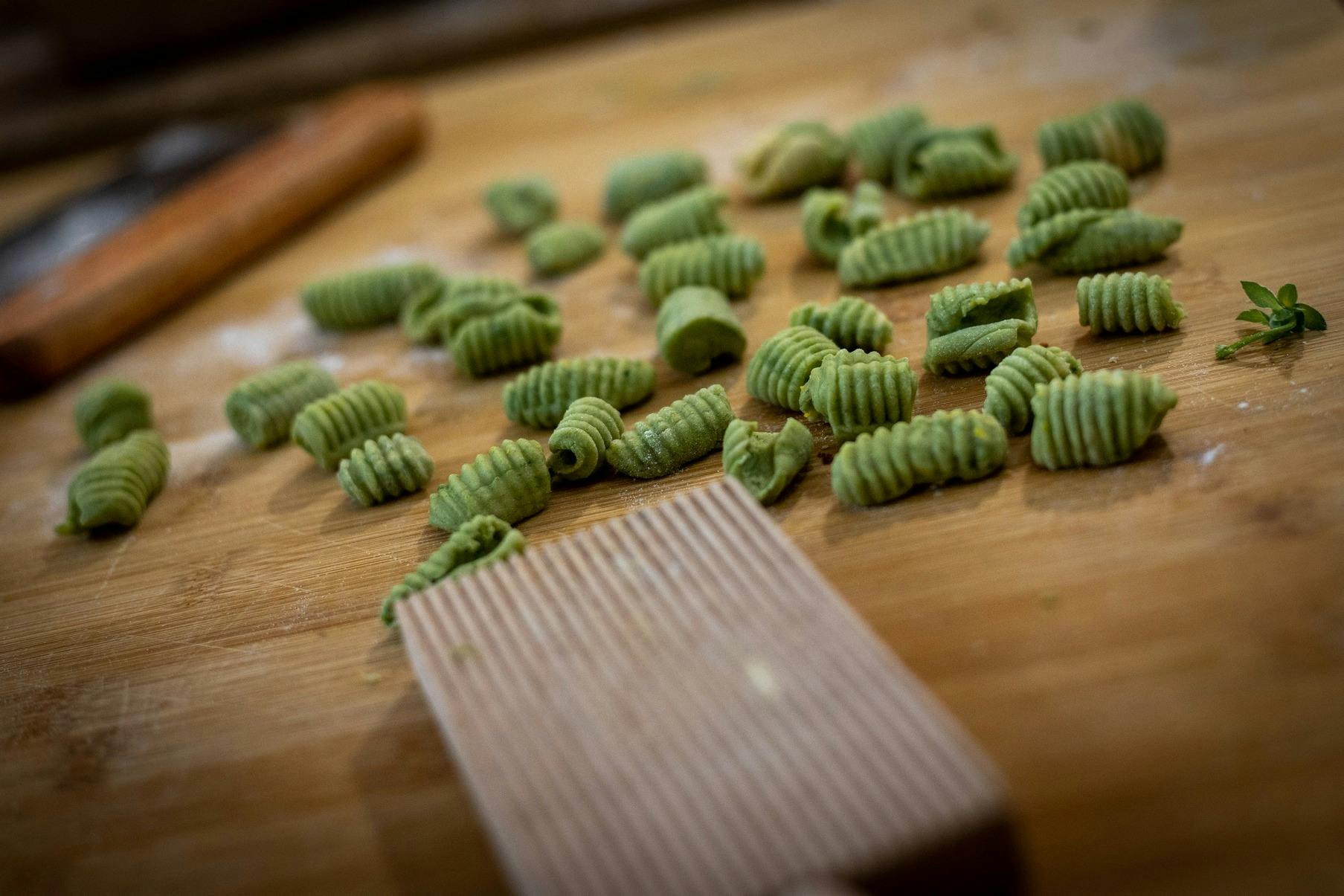 Trossos de pasta verda de gnocchi escampats sobre una superfície de fusta al costat d'un tauler de pasta amb crestes.