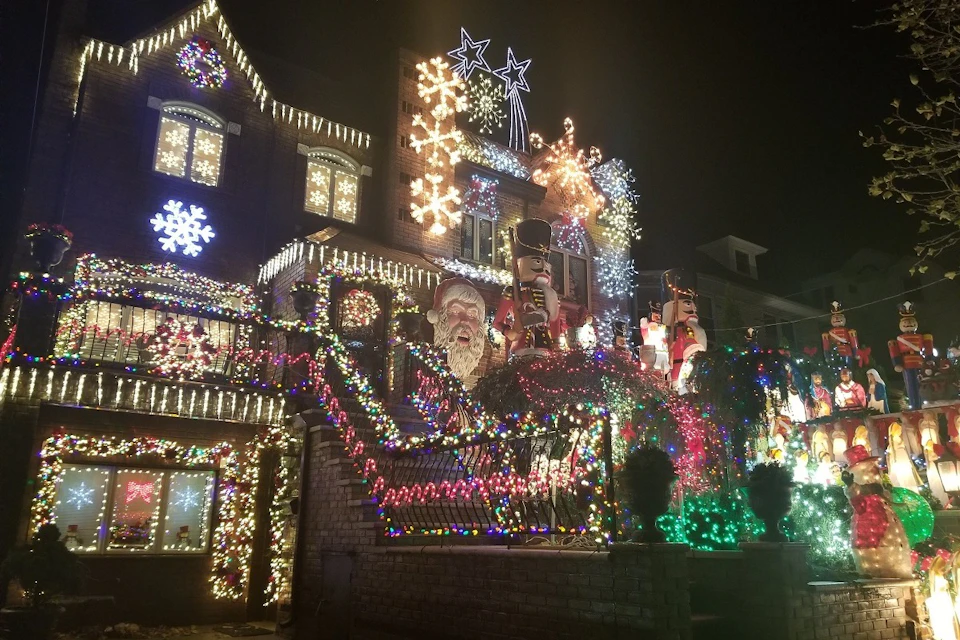 A house elaborately decorated with Christmas lights, ornaments, and figures including Santa and nutcracker soldiers at night.