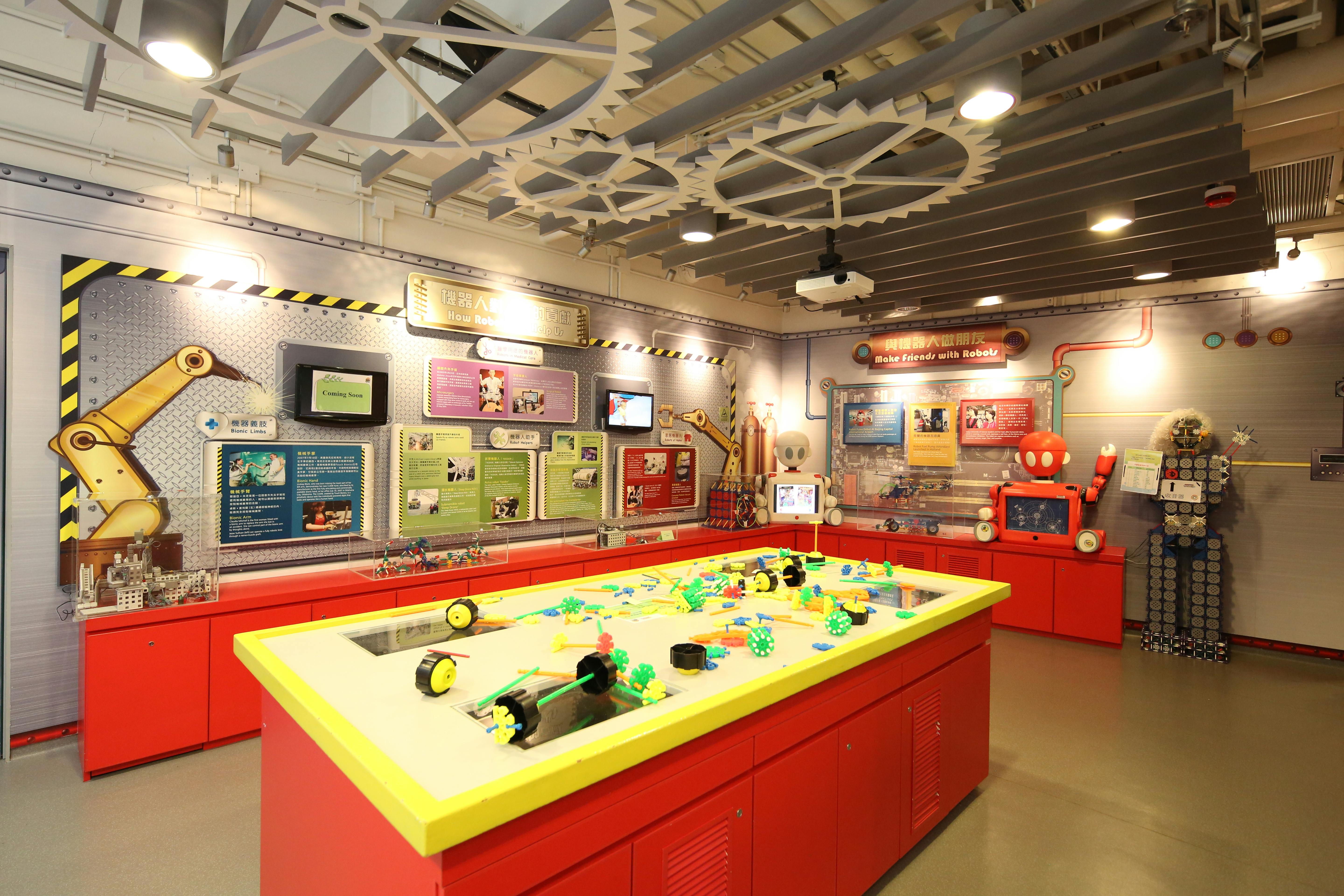 Светлая образовательная комната с красными верстаками, красочными инструментами, настенными экспонатами и большими украшениями на потолке.