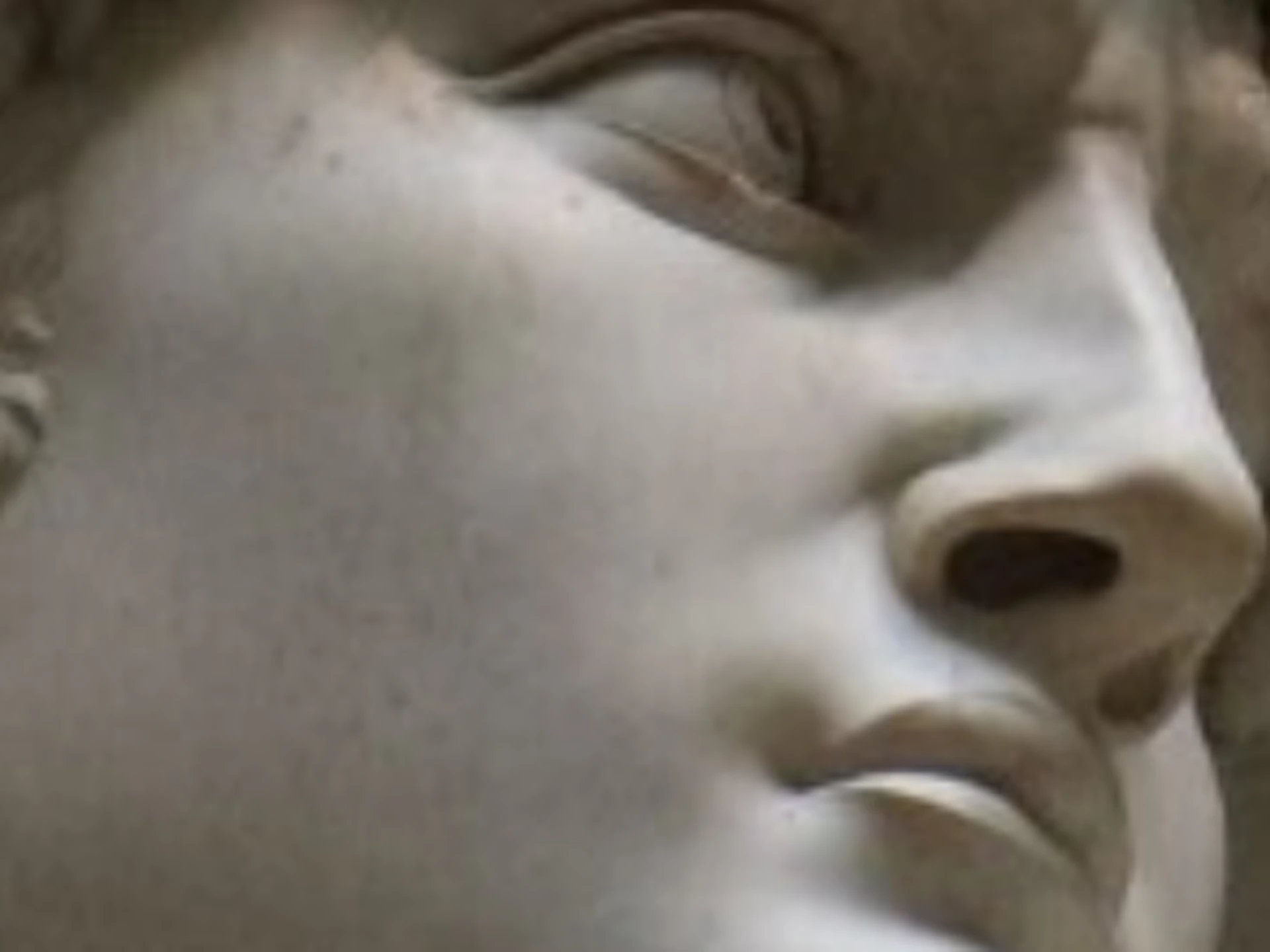 A hand holding a smartphone displays information about Michelangelo's statue of David, with the actual statue visible in the background.