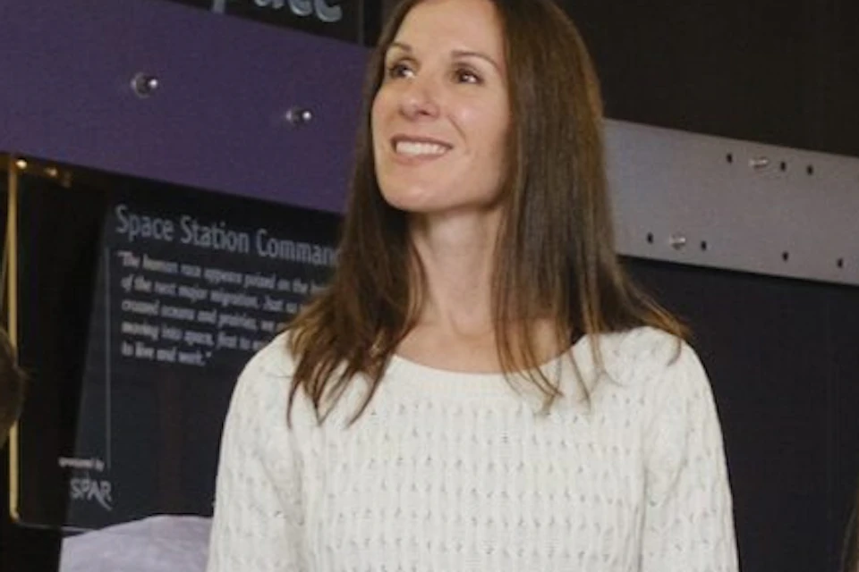 A woman and two children stand inside a space-themed exhibit with astronaut displays and interactive panels on the walls.