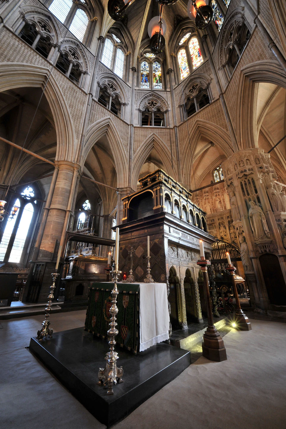 Intricate interior of a Gothic cathedral with vaulted arches, ornate altar, tall candles, and decorative stained glass windows.