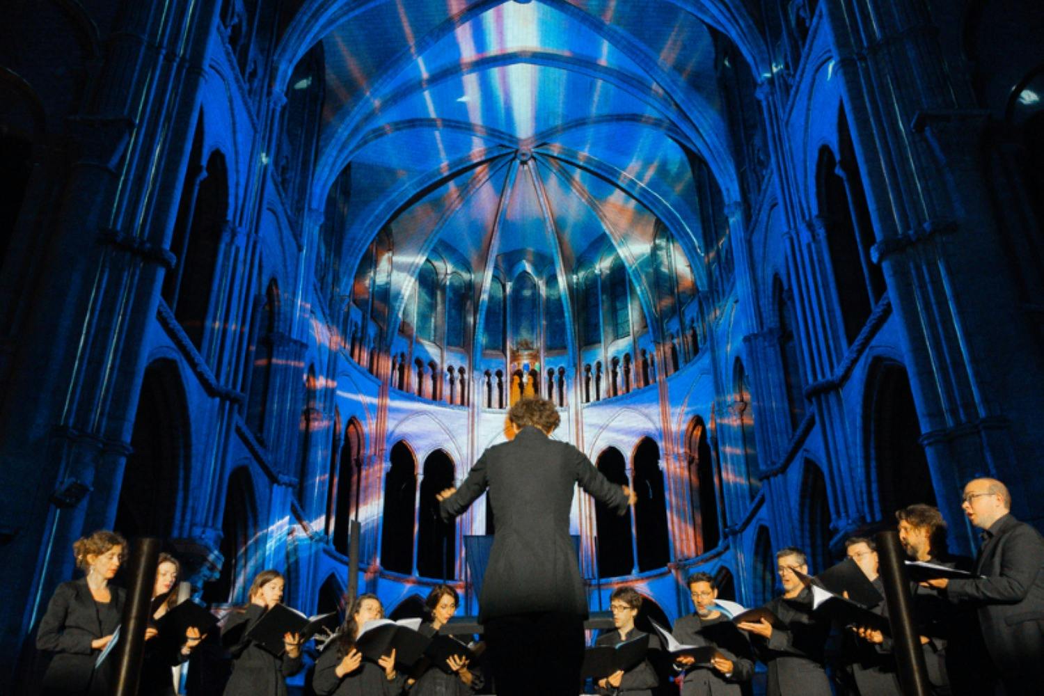 A choir performing in a cathedral with colorful light projections on the walls and ceiling.