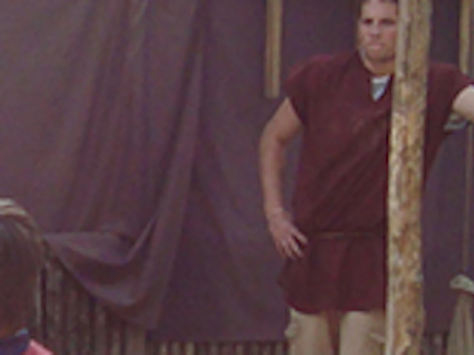 Group of people dressed in ancient Roman attire, with two engaging in a practice sword fight, and three others observing.