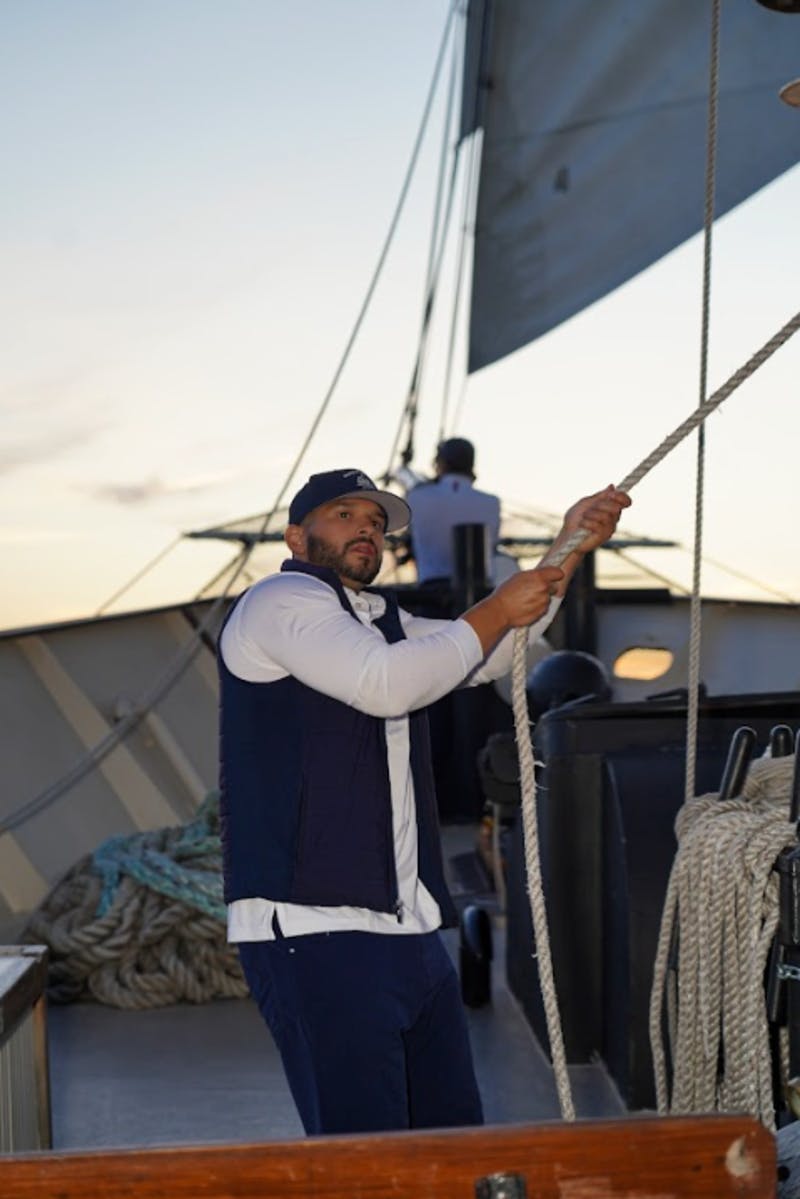 A person on a sailboat is pulling on a rope, with another person in the background at dusk.