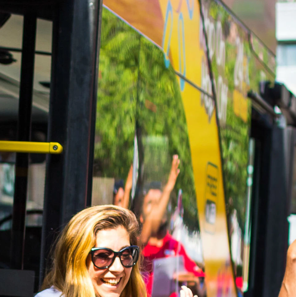 A cheerful bus attendant high-fives a young boy while a man carries another boy on his shoulders, and a woman stands beside them.