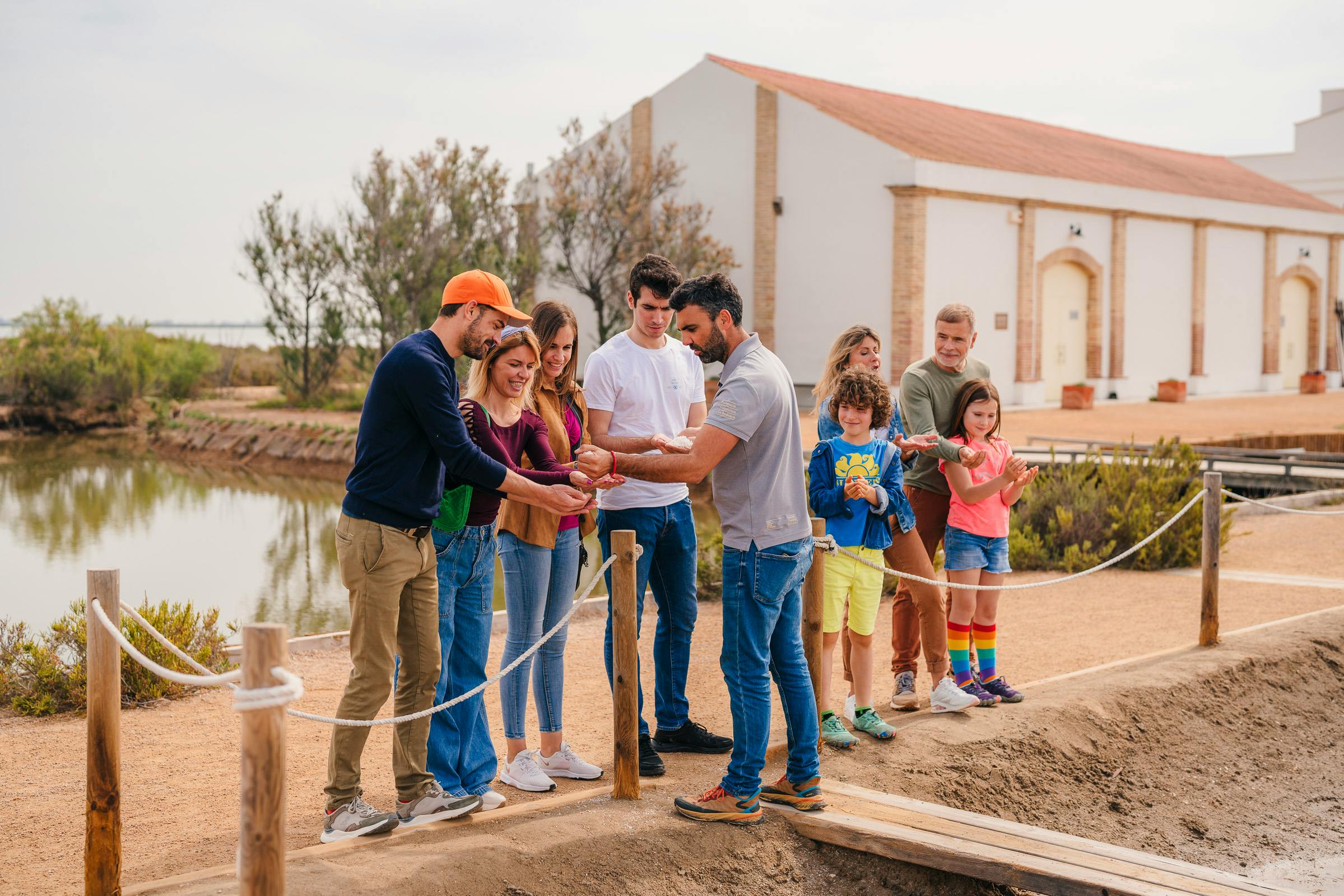 Μια ομάδα ενηλίκων και παιδιών παρατηρούν έναν άνδρα να εξηγεί κάτι κοντά σε μια μικρή γέφυρα σε ένα ιστορικό περιβάλλον.