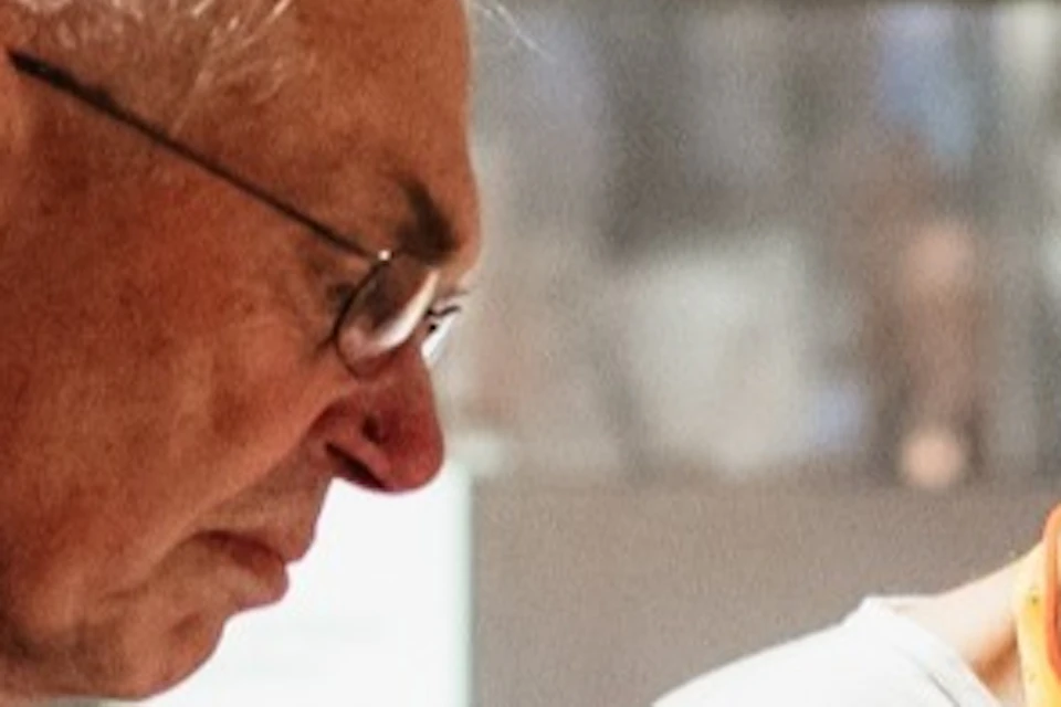A museum guide explains an exhibit to two visitors in a well-lit gallery with a detailed display on a wall.