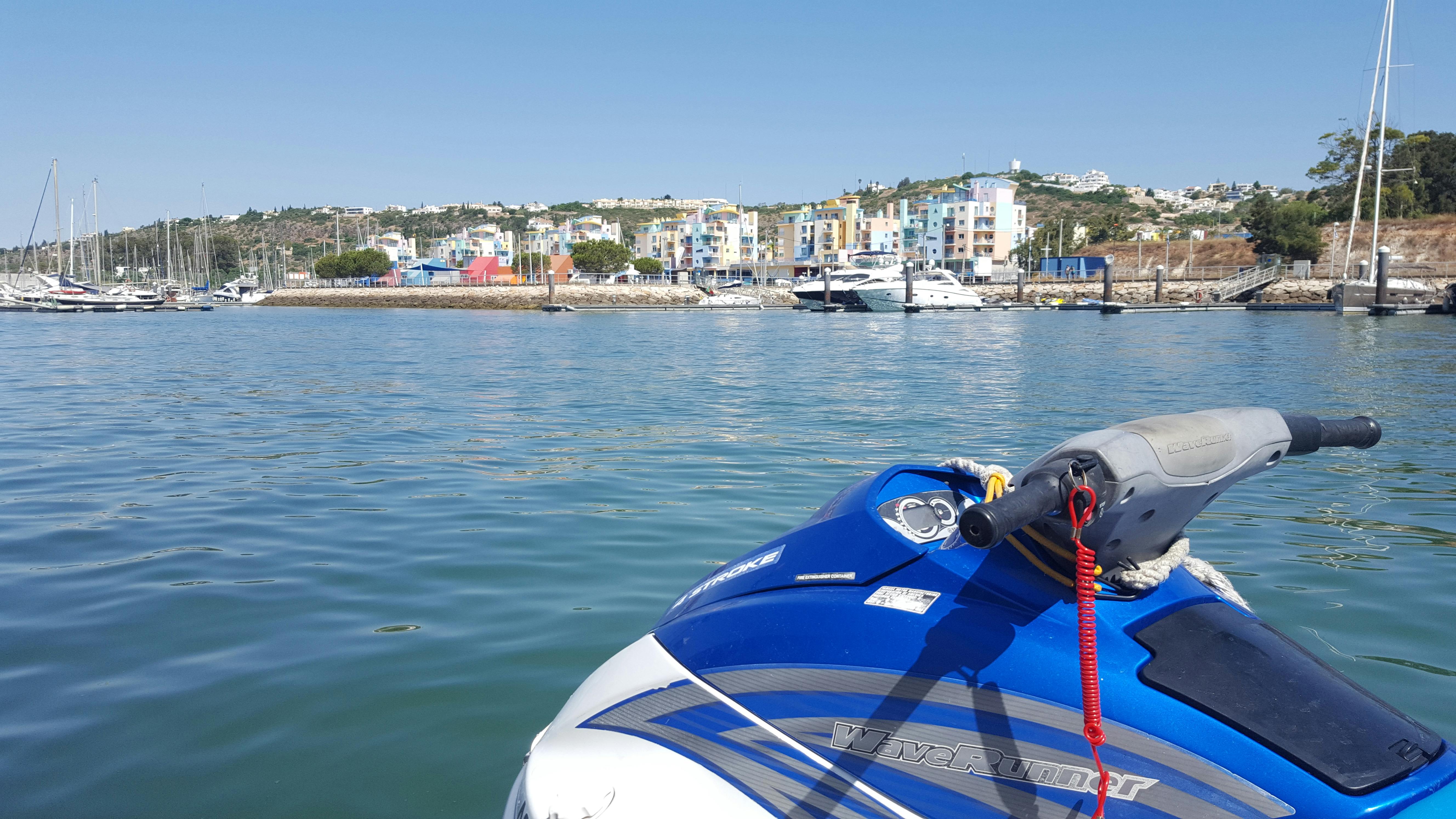 ボートとカラフルな建物を背景にしたマリーナの近くに、青と白のジェットスキーが浮かんでいます。 上の空は青く澄んでいます。