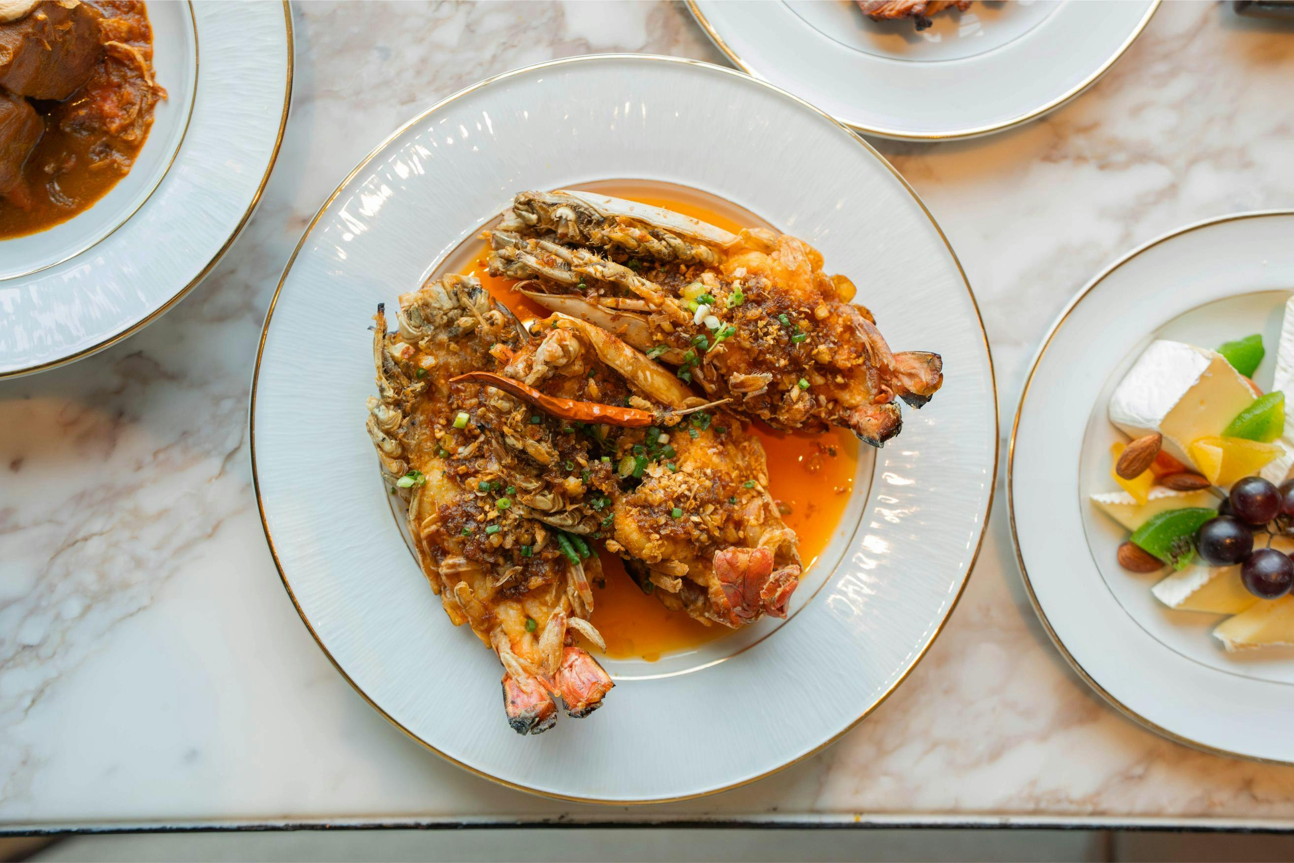 A plate of cooked prawns with a savory sauce, garnished with herbs, served on a white dish with a gold rim.