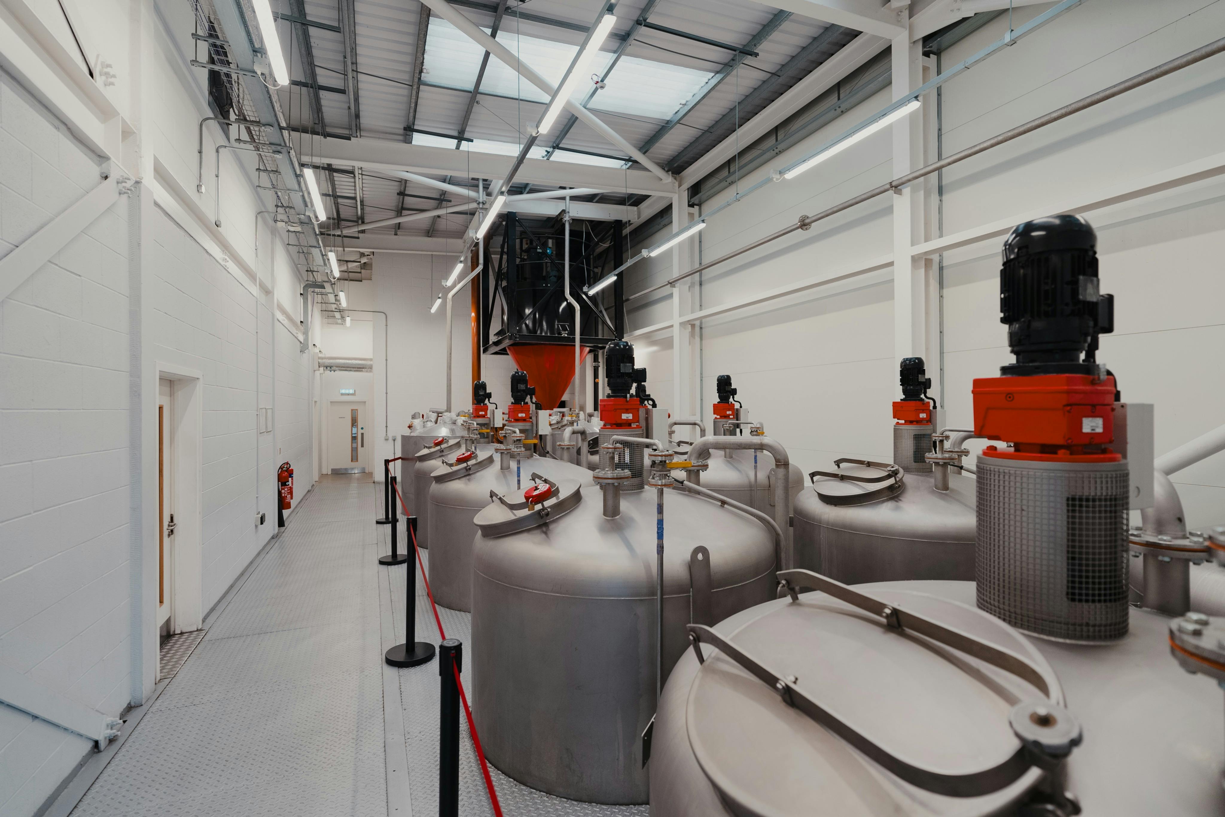 Et moderne industrianlæg med store metaltanke, rødt udstyr og loftsbelysning i et rummeligt, rent miljø.