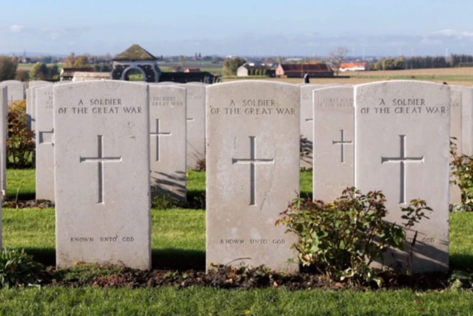 Rows of white tombstones inscribed "A Soldier of the Great War" in a cemetery with greenery and distant buildings.