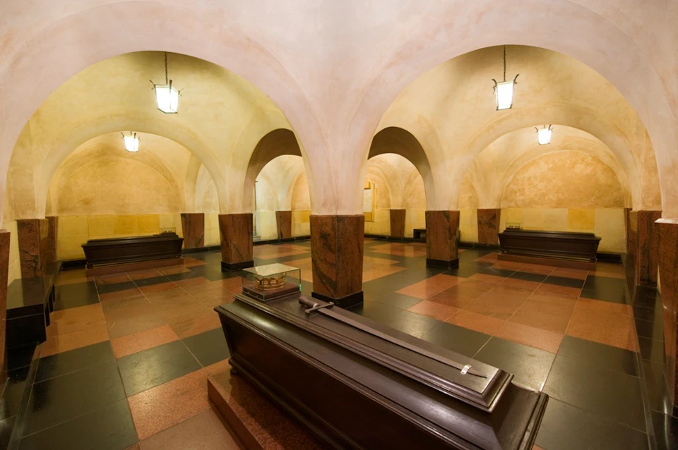A crypt with arched ceilings, multiple tombs, and hanging lanterns on the walls, creating a solemn atmosphere.