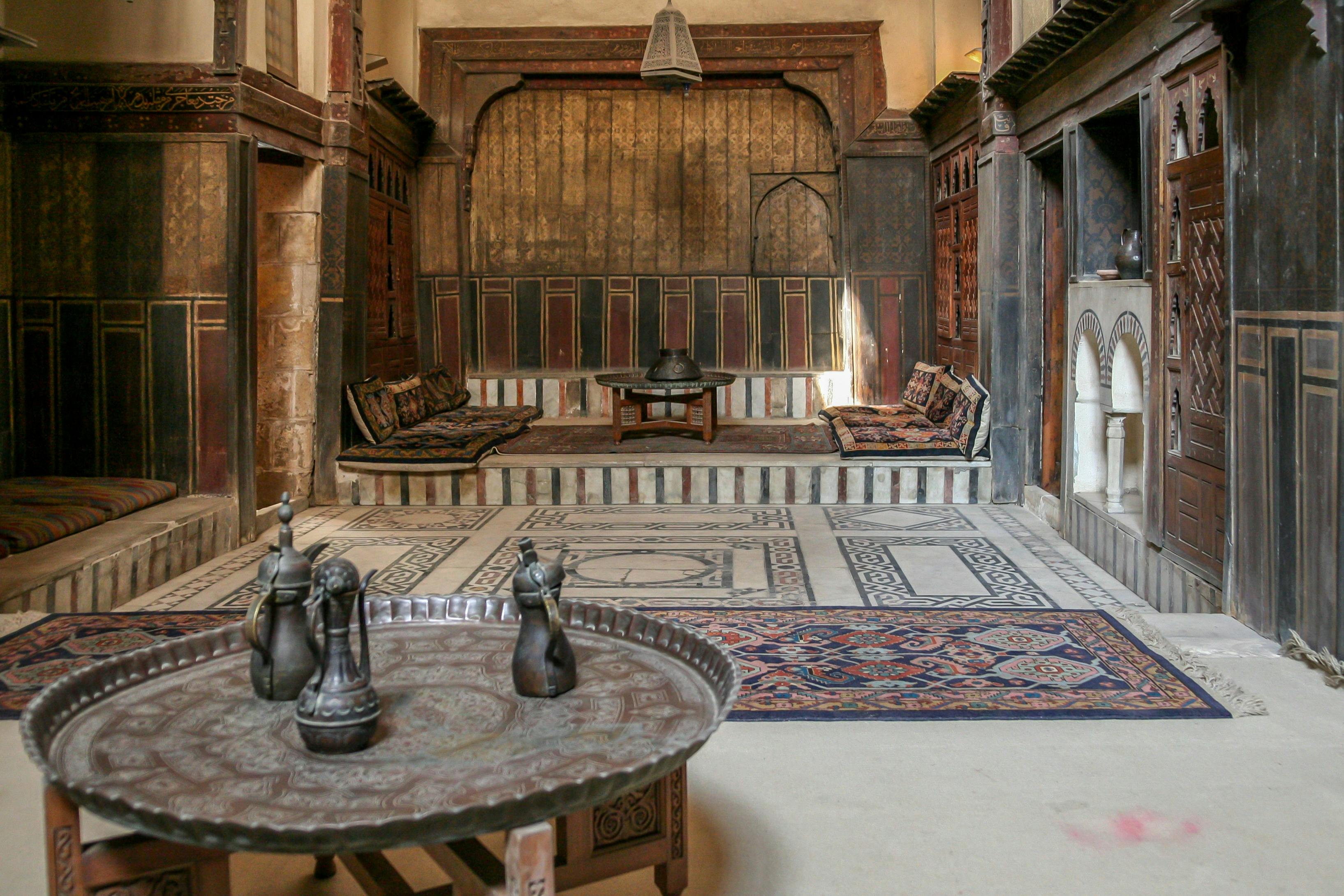 Украшенная комната с мягкими зонами отдыха, центральным низким столом, металлическими кувшинами на круглом подносе и узорчатыми ковриками.