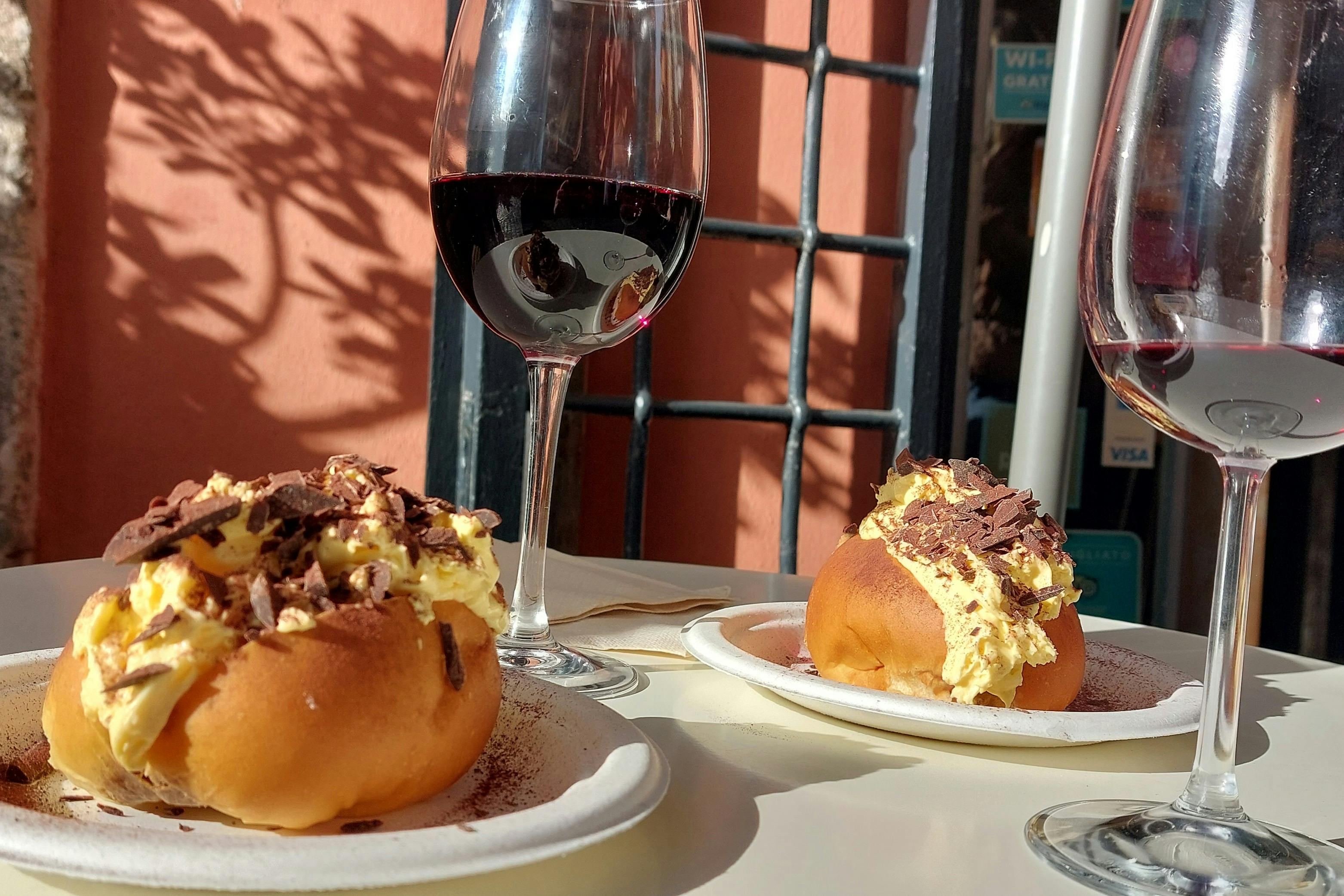 Two plates of pastries with cream and chocolate shavings, paired with glasses of red wine, on an outdoor table.