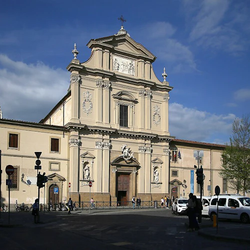 En utsmyckad kyrkfasad med statyer och detaljerade sniderier under en blå himmel, med fotgängare och bilar i förgrunden.