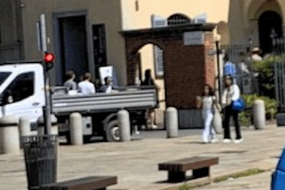 A group of people with red bicycles stands in a plaza with historic buildings in the background.