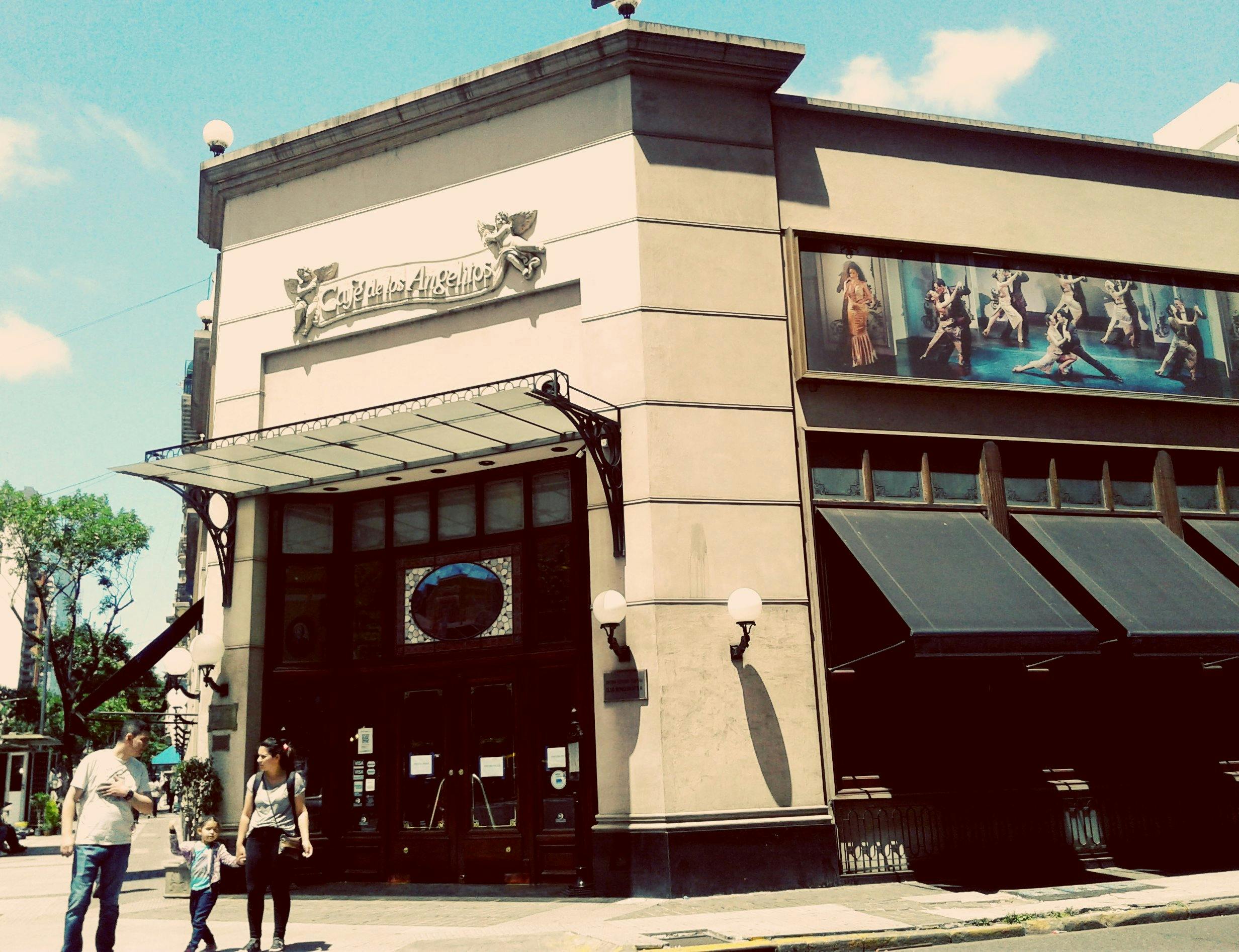 Entrance of a building with a "Café de los Angelitos" sign, featuring a woman and child walking past.