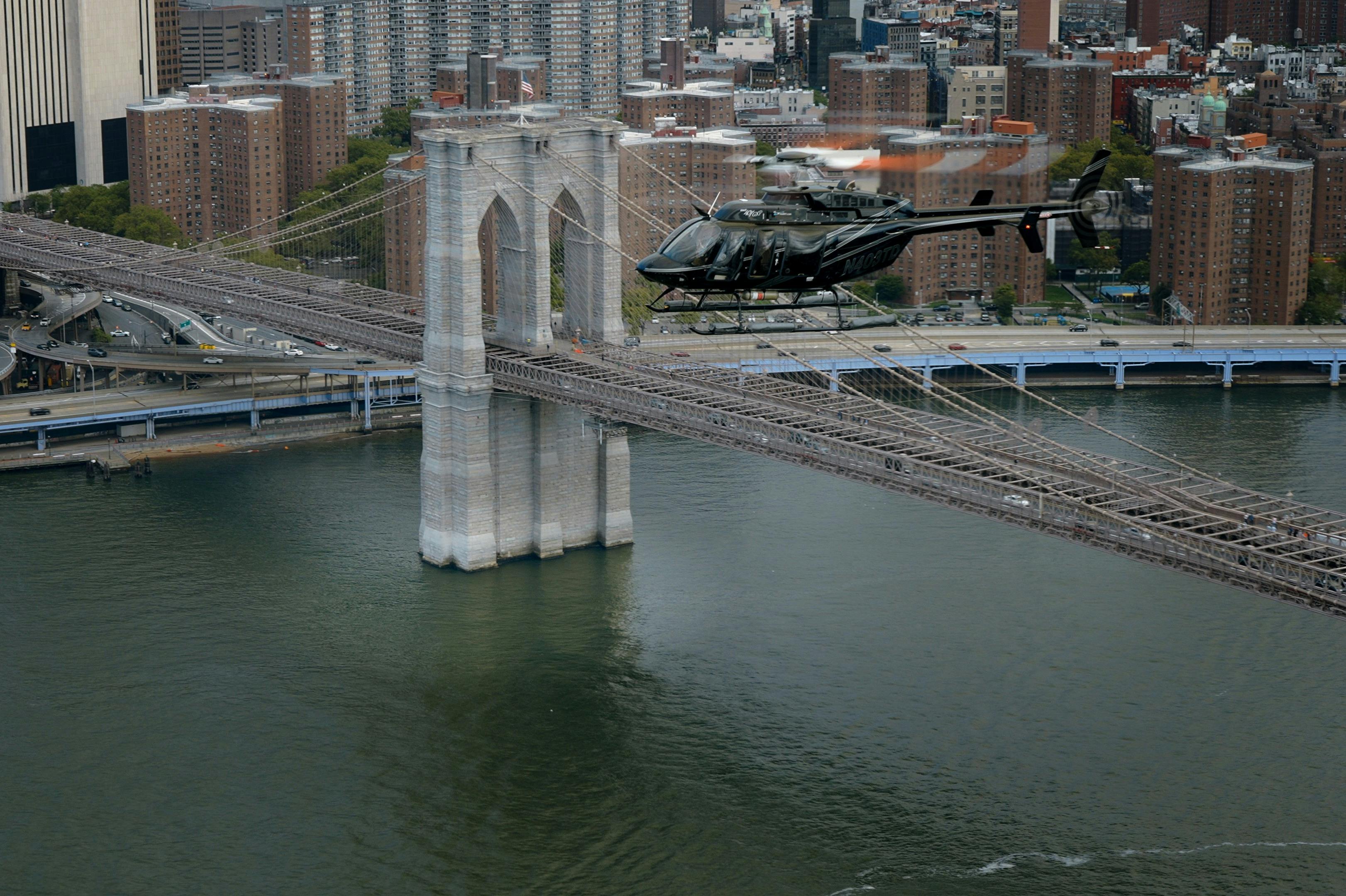 도시 풍경과 강을 배경으로 브루클린 다리 위로 헬리콥터가 날아갑니다.