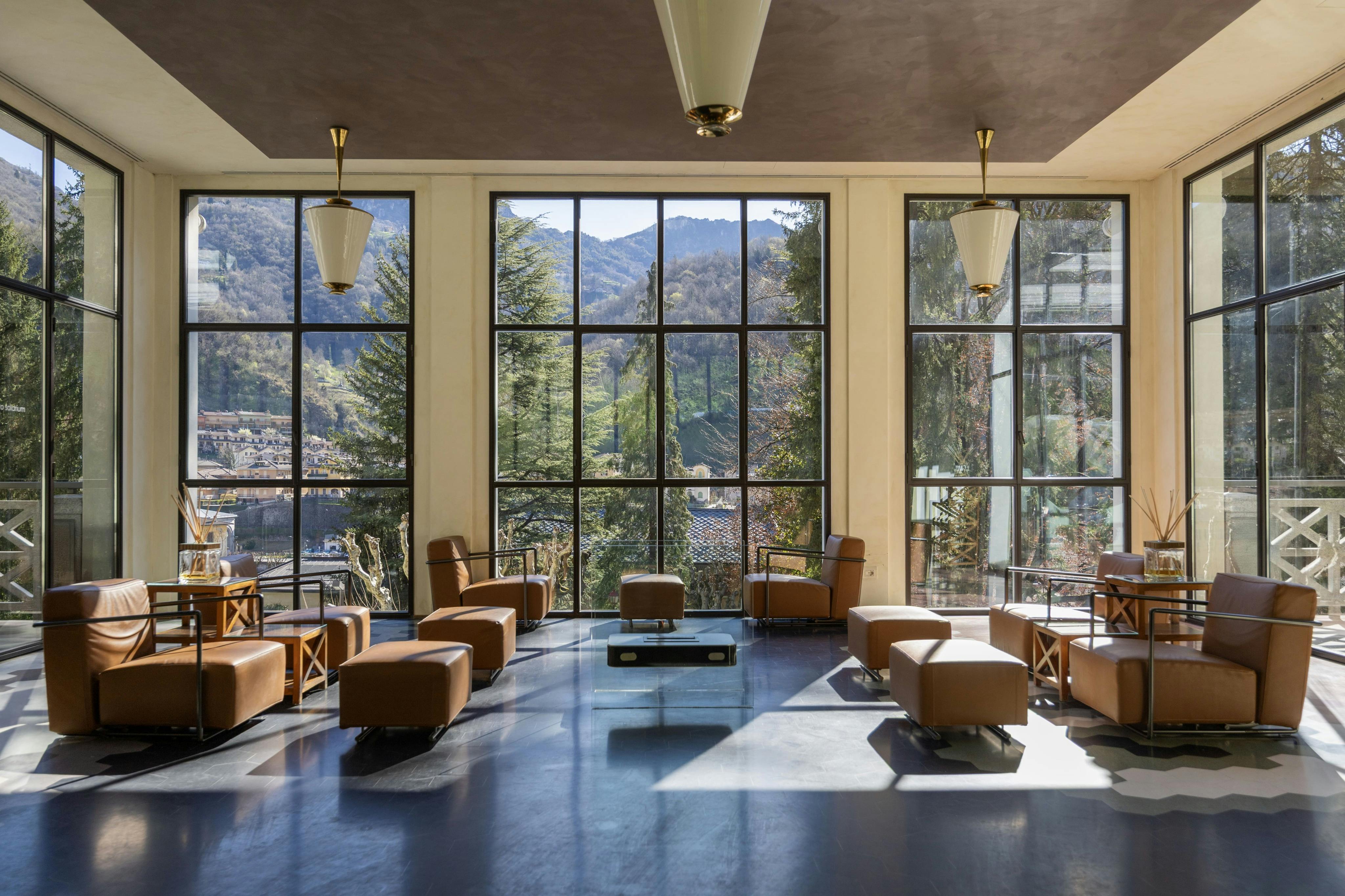 Un salone moderno con grandi finestre che mostrano una vista panoramica sulle montagne, con sedie in pelle e luci a sospensione.