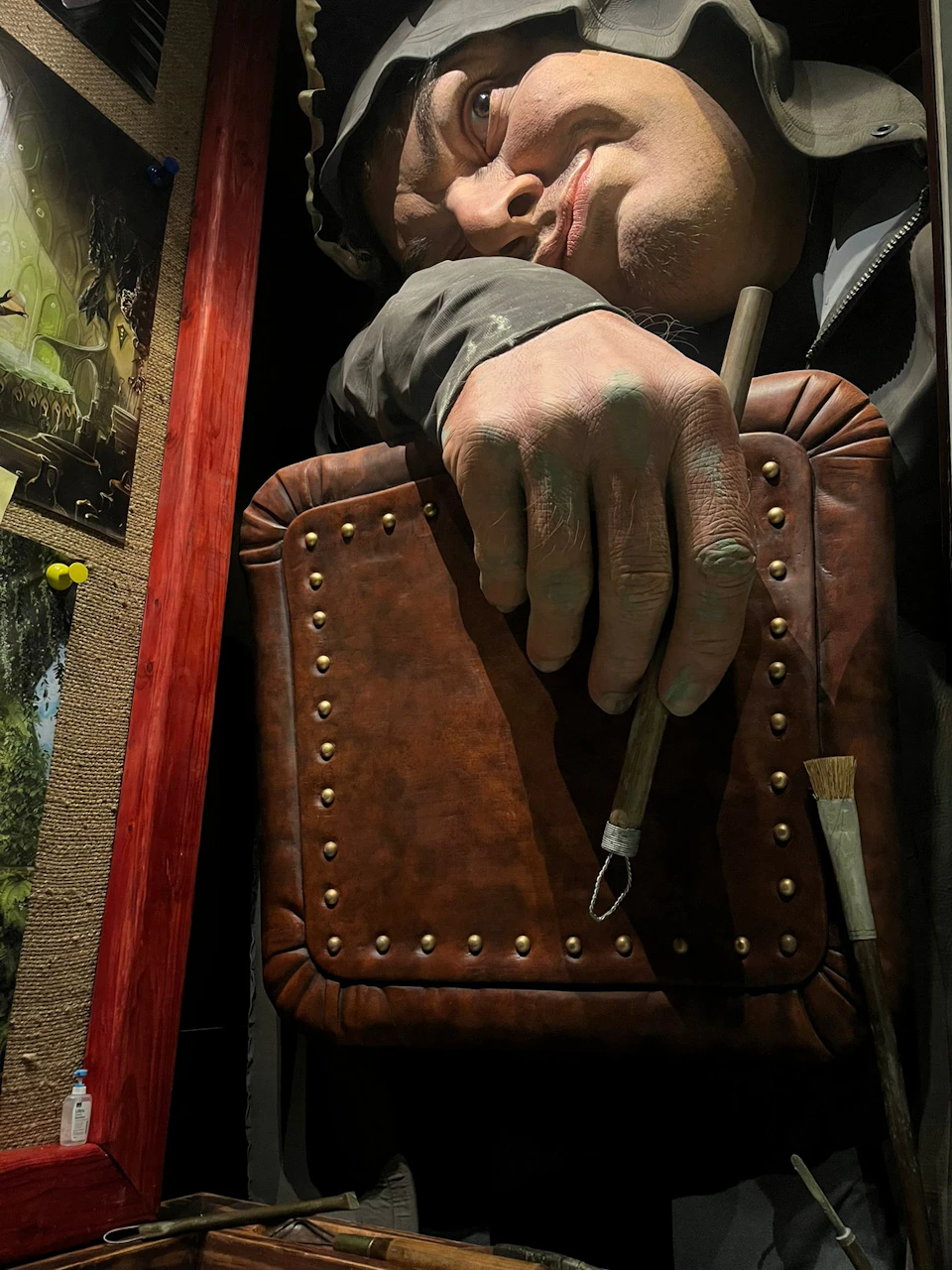 A close-up of a sculpture of a person holding a brown leather bag and a paintbrush, with detailed hand and face features.