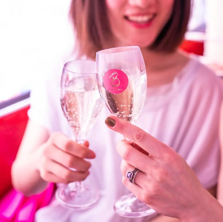 Two people clinking champagne glasses, one hand with a ring, one glass marked with a pink sticker.
