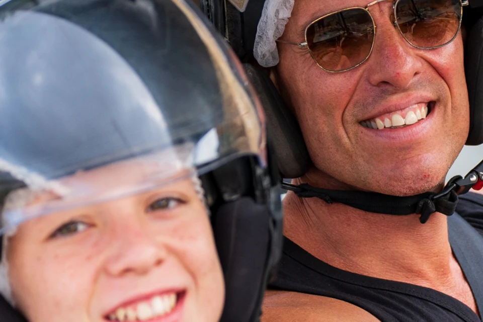 Two people wearing helmets sitting in an off-road vehicle, smiling and enjoying the moment.
