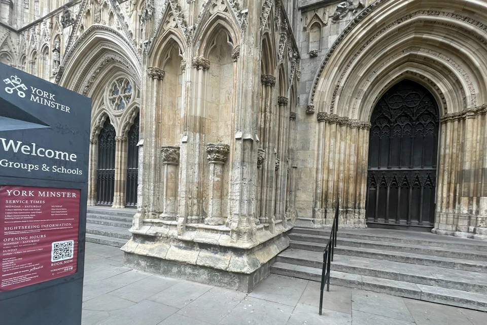 Ornate Gothic cathedral entrance with pointed arches, intricate carvings, and steps leading to dark wooden doors.