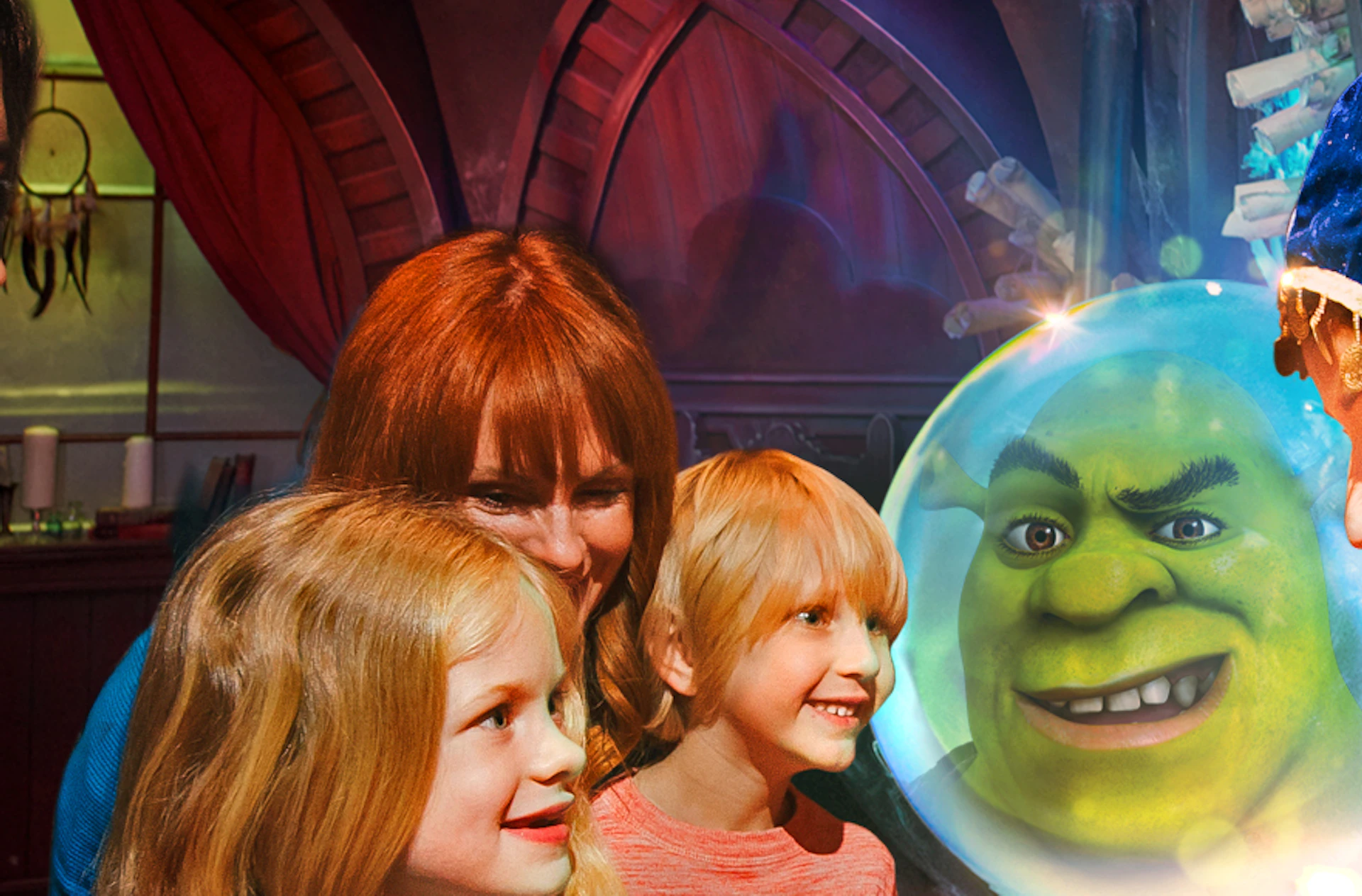 Children and adults interact with a woman in colorful costume near a glowing crystal ball displaying a character's face.