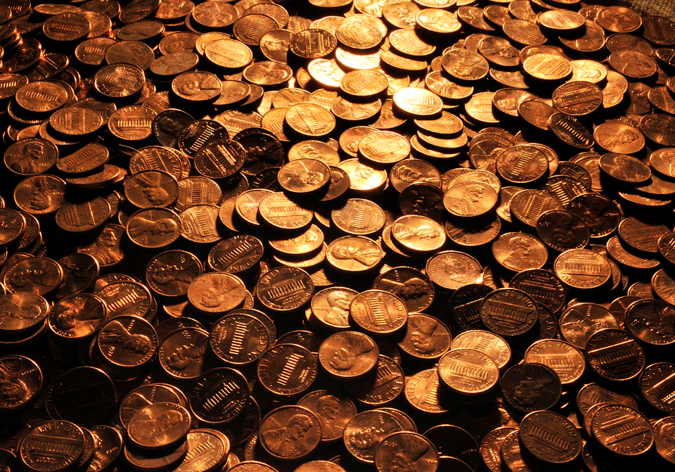 A large pile of shiny U.S. pennies, showing both heads and tails, reflecting a warm, golden light.