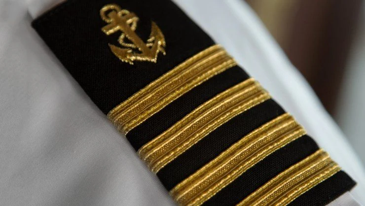 Close-up of a navy officer's uniform shoulder strap featuring four gold stripes and an embroidered anchor insignia on a black background.