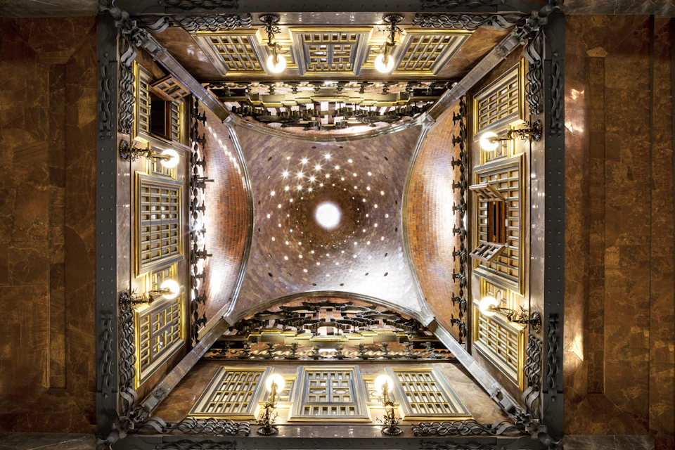 A symmetrical shot of an ornate, vaulted ceiling with decorative lights, windows, and intricate architectural detailing.