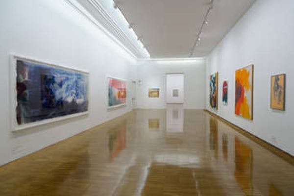 A modern art gallery with polished wooden floors and large abstract paintings hanging on white walls.