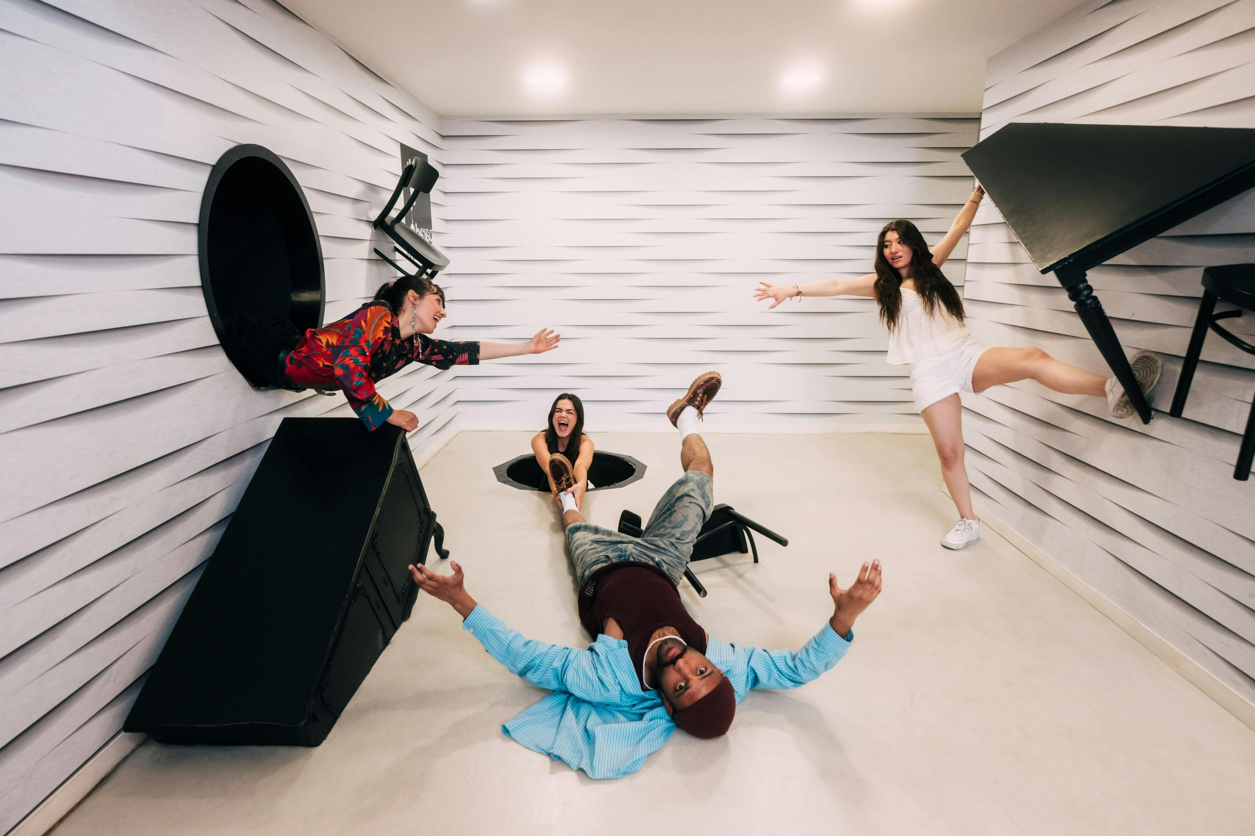 視覚的な錯覚を持つ遊び心のある傾斜した部屋で、床のように設計された壁を備えた4人の人物が交流しています。