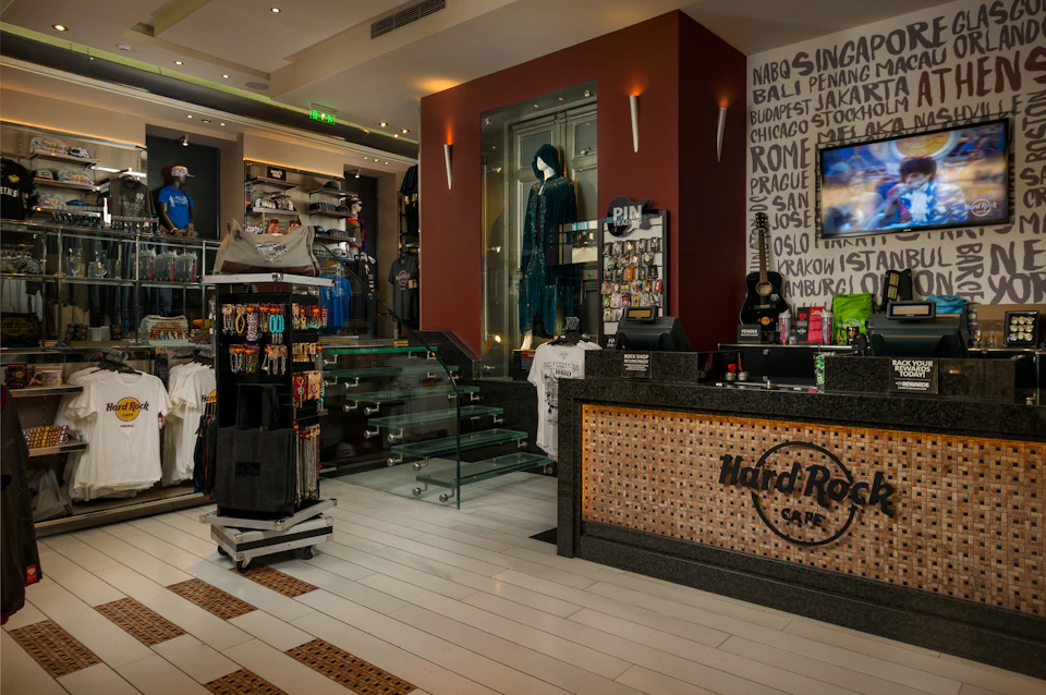 Interior of a Hard Rock Café shop with merchandise, a display case with a blue outfit, and a reception counter.