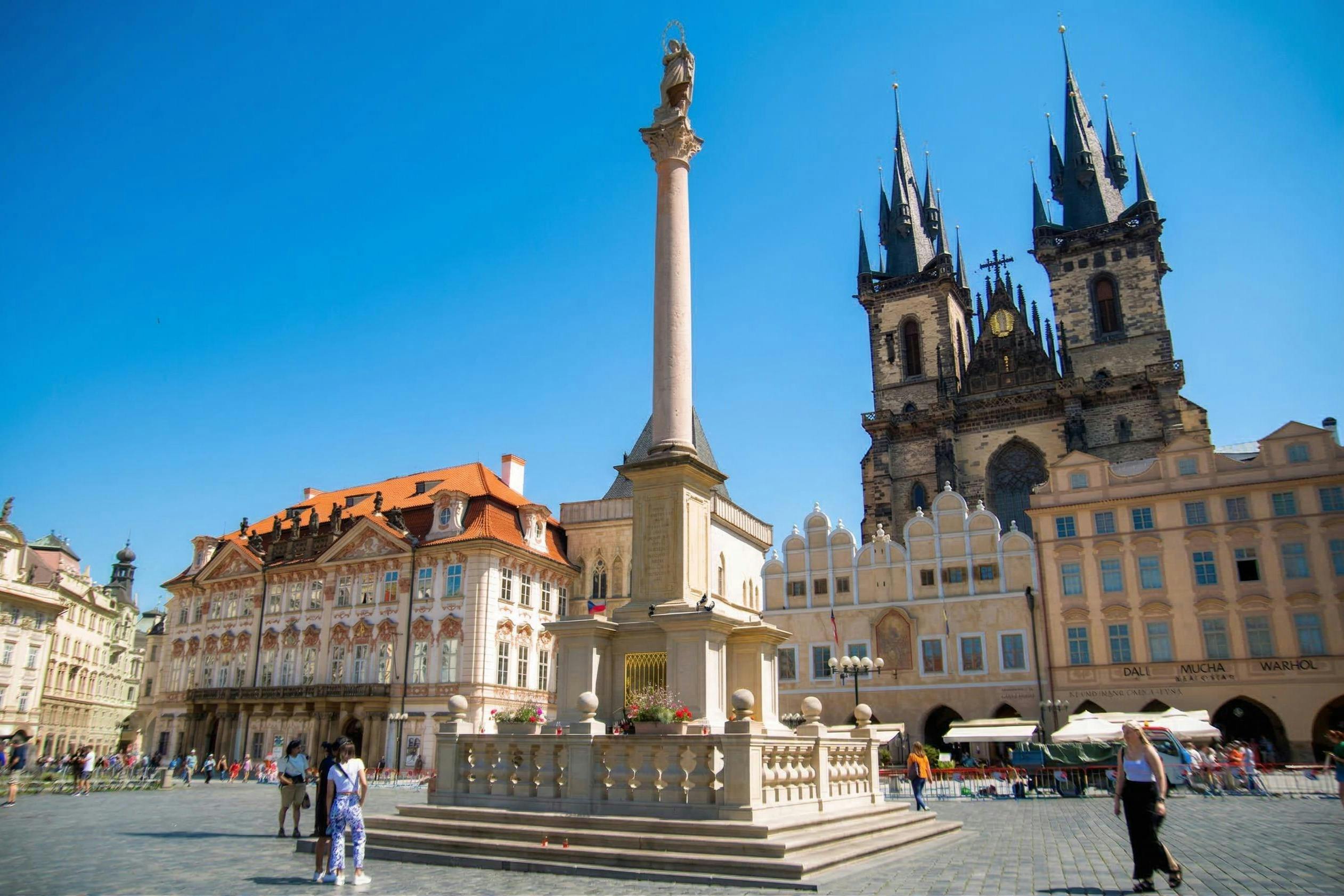 广场上有圆柱纪念碑、历史建筑和清澈蓝天下的尖顶教堂。