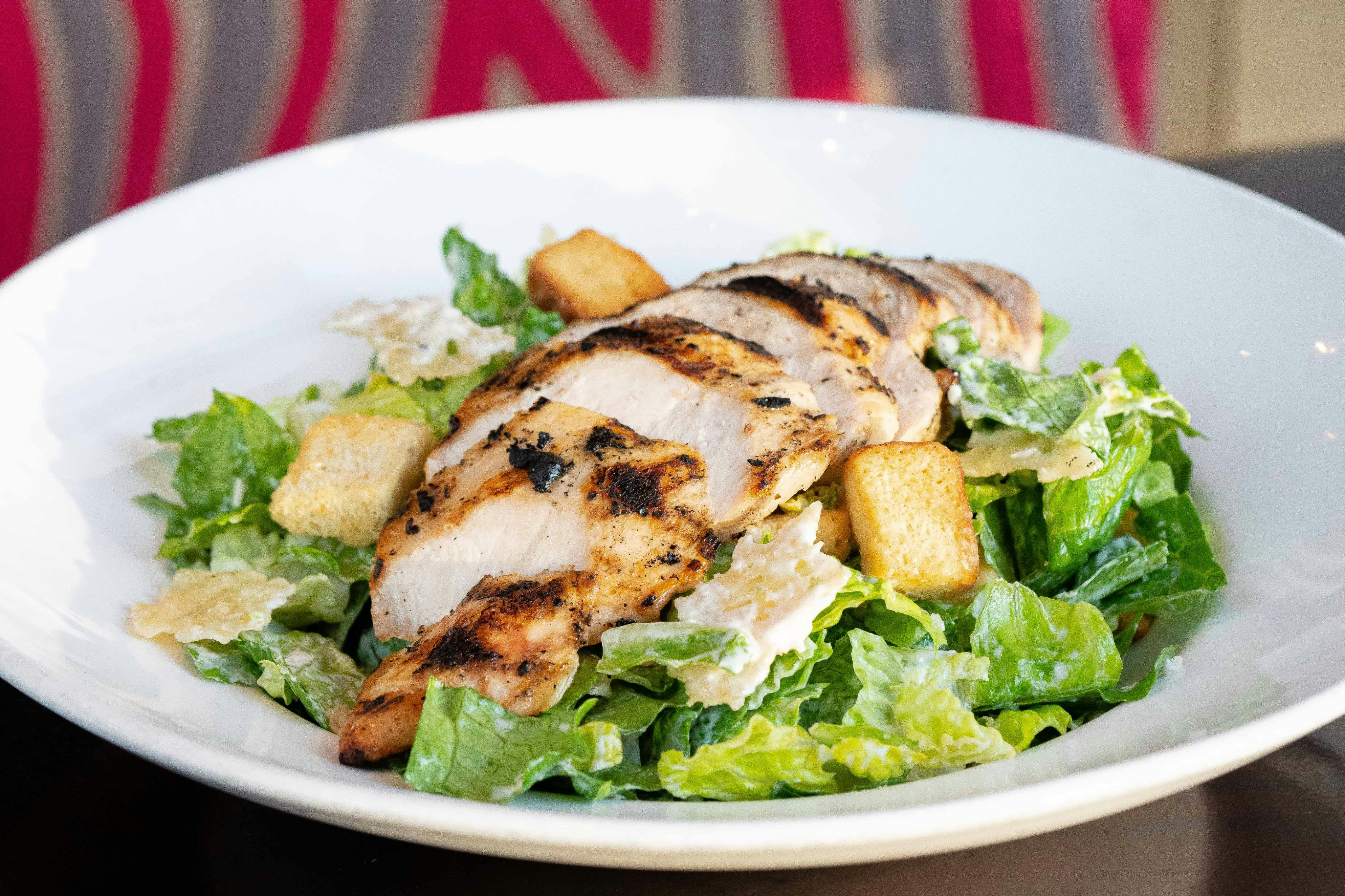 Στήθος κοτόπουλου στη σχάρα σε ένα κρεβάτι από μαρούλι romaine, κρουτόν και σάλτσα Caesar σε ένα λευκό μπολ.