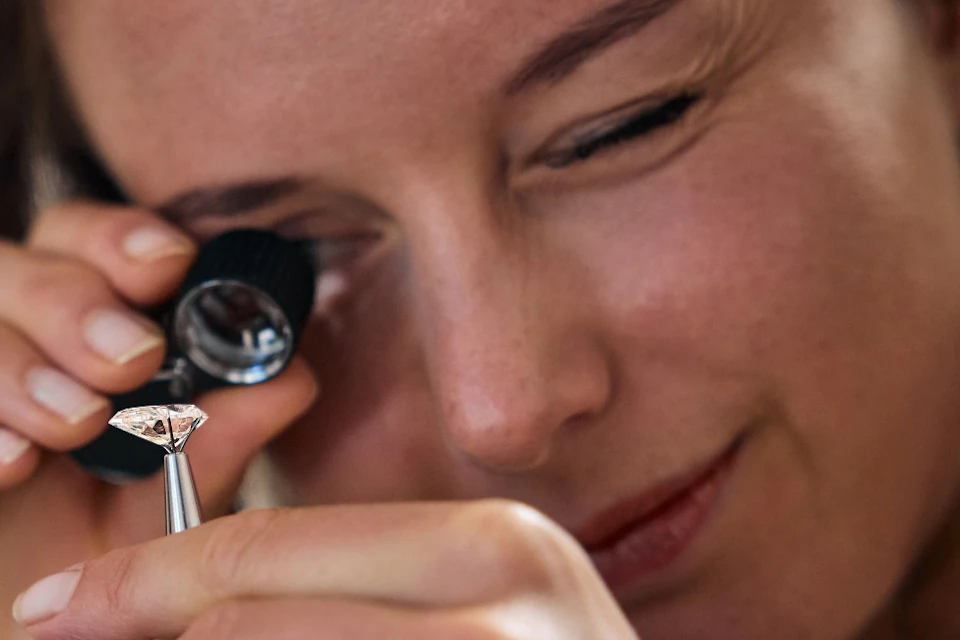 A person examining a diamond with a loupe, holding it carefully with a tool, focused on evaluating its quality.