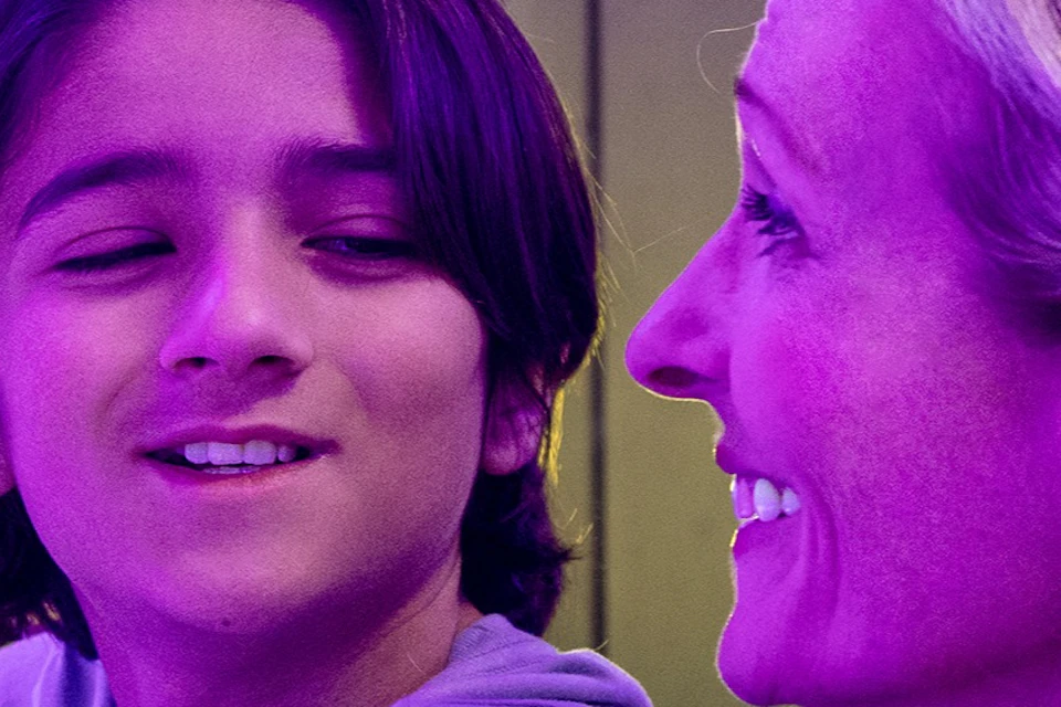 A woman and a child smiling at each other in a place with purple lighting and reflective surfaces.